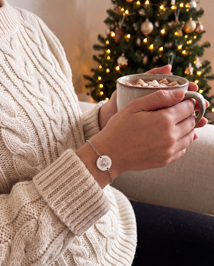 Woman wearing the dog portrait chain bracelet holding hot cocoa by a Christmas tree