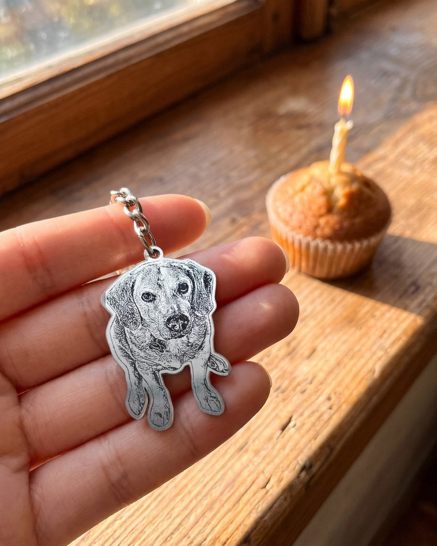 Engraved beagle photo keychain held in a hand by a sunny windowsill with a birthday cupcake
