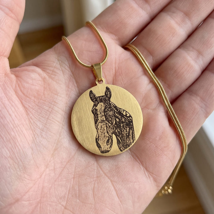 round pet photo necklace with an engraved pet portrait, held in a hand to show true size
