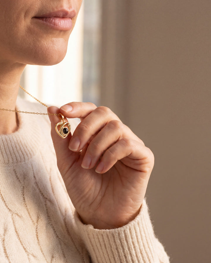 Woman in a cream sweater lifting her gold heart photo projection necklace