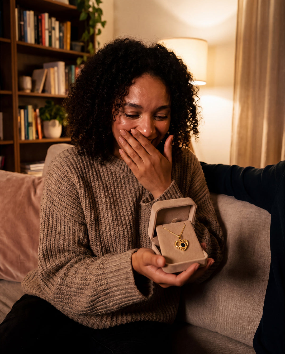 Woman covering her mouth in happy surprise as she opens a heart projection necklace gift