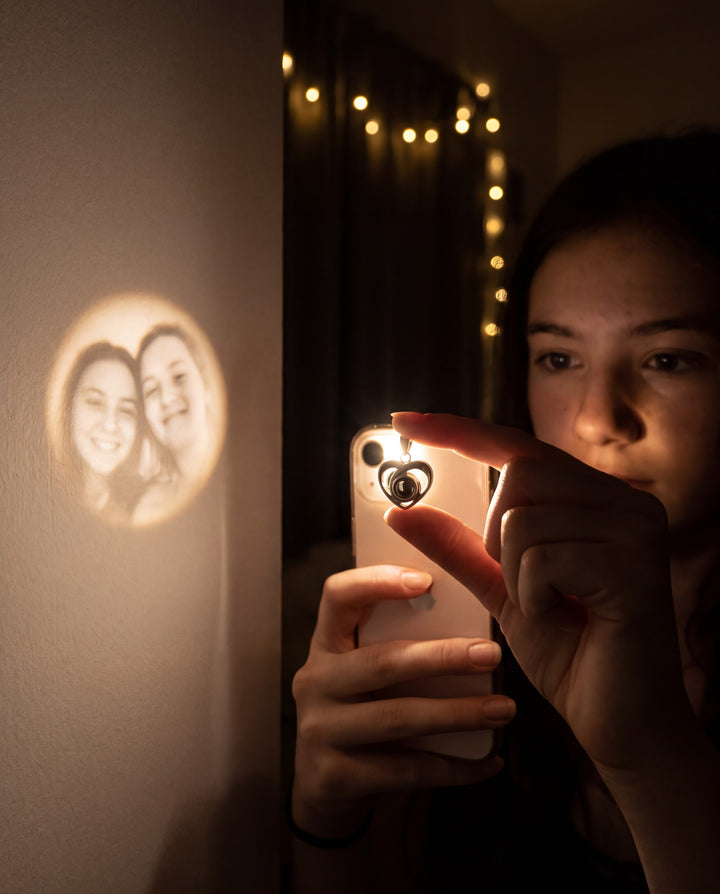 Teen shining a phone light through her heart necklace to project a soft photo on the wall