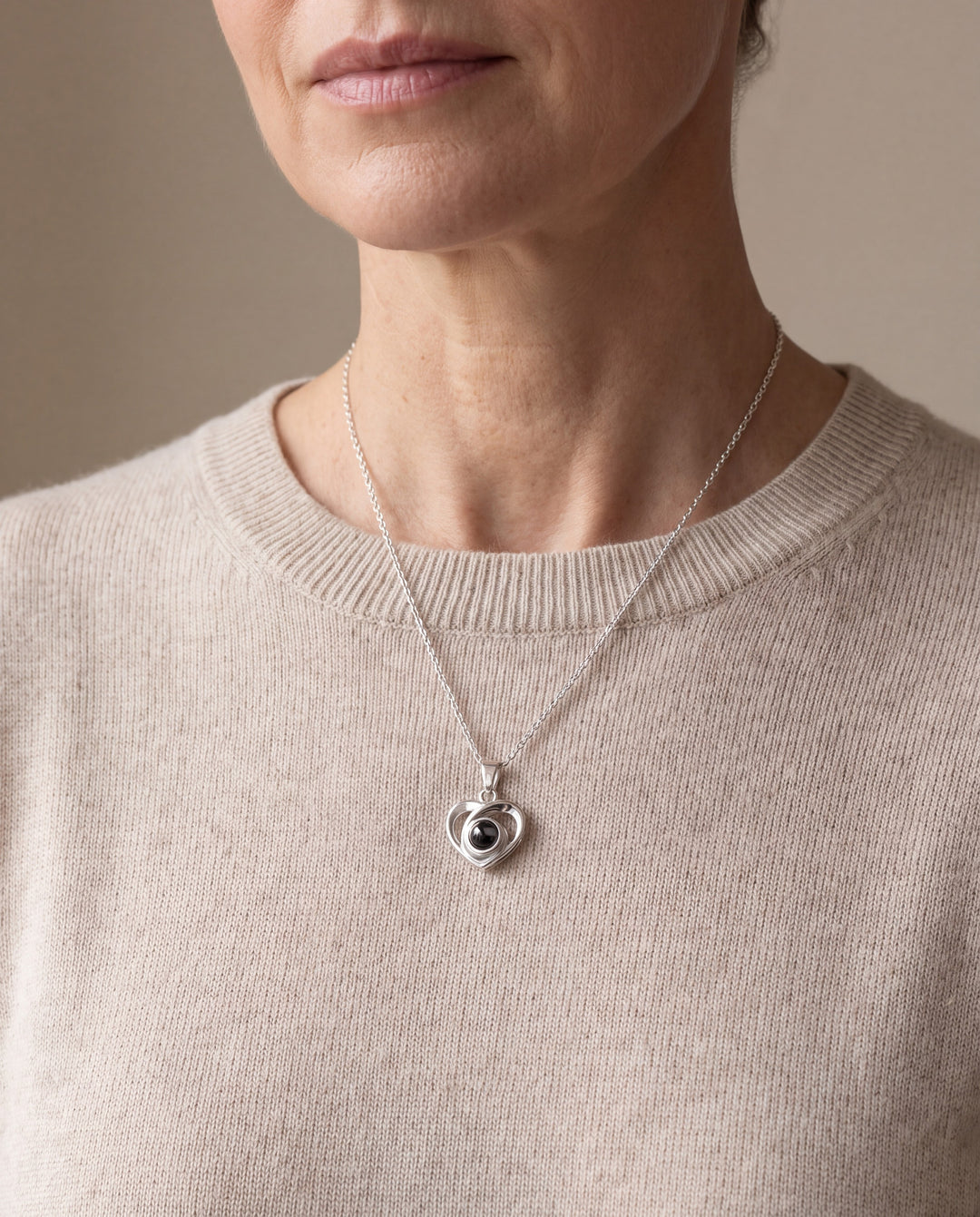 Woman wearing the silver heart projection necklace with an oatmeal sweater