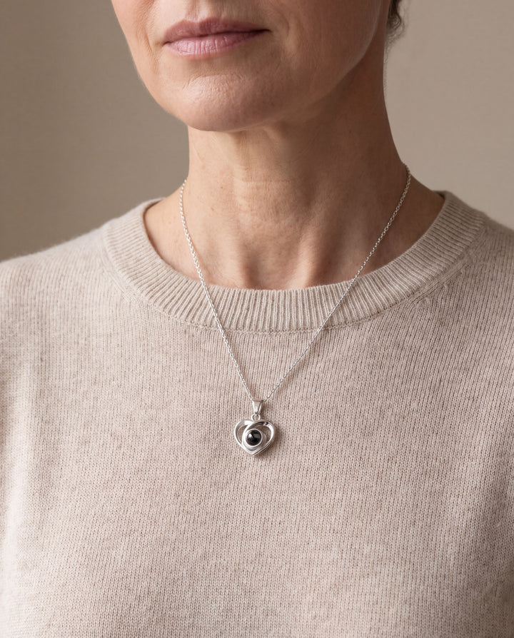 Woman wearing the silver heart projection necklace with an oatmeal sweater