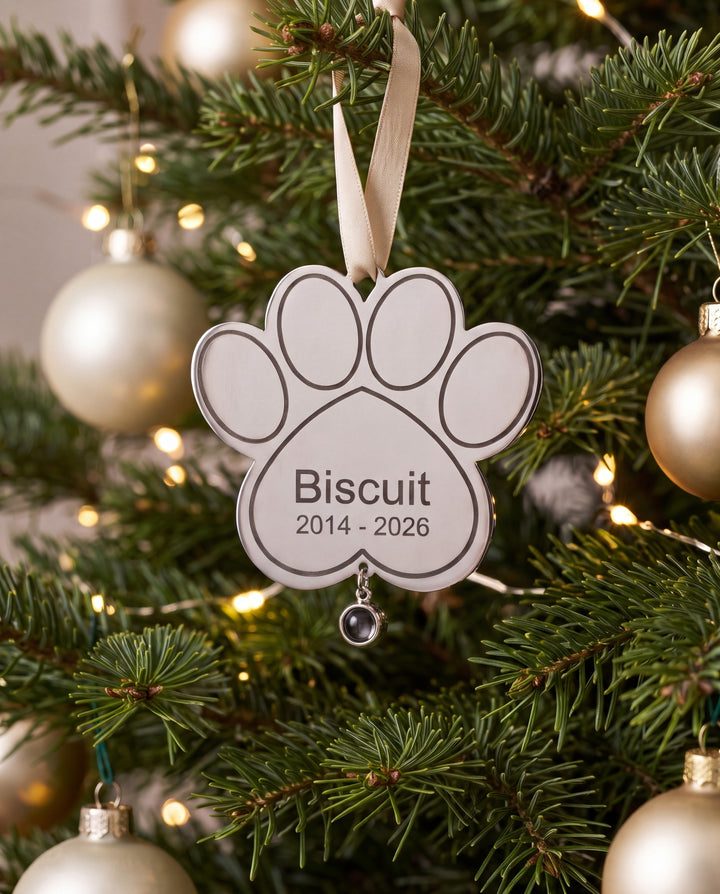 Engraved paw memorial ornament with pet name hanging on a Christmas tree
