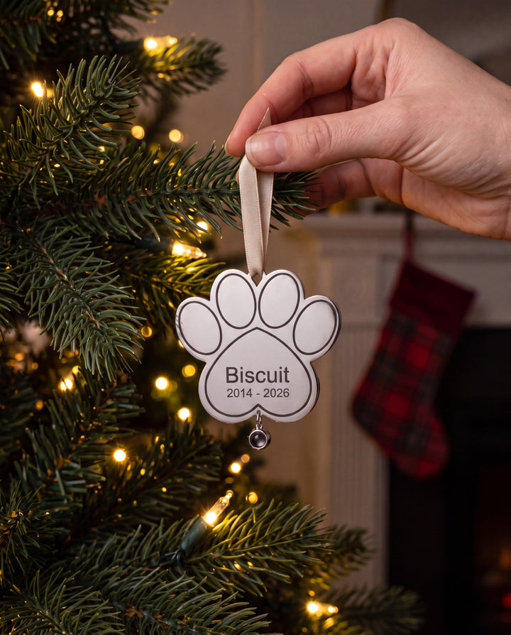 Hand hanging the engraved paw ornament on a Christmas tree by the fireplace