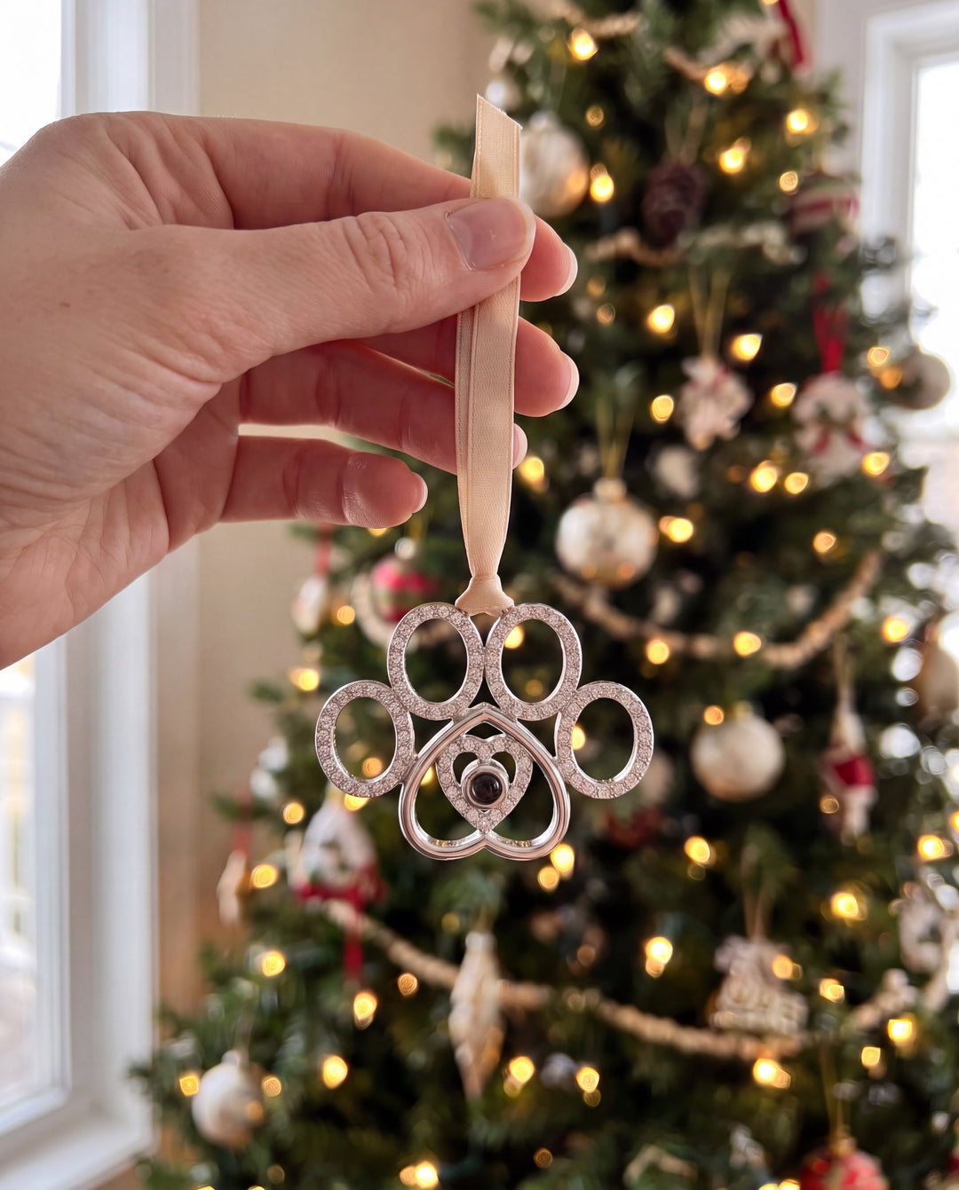 Hand holding the crystal paw ornament in front of a lit Christmas tree