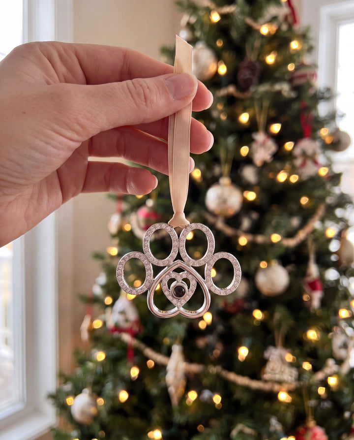 Hand holding the crystal paw ornament in front of a lit Christmas tree