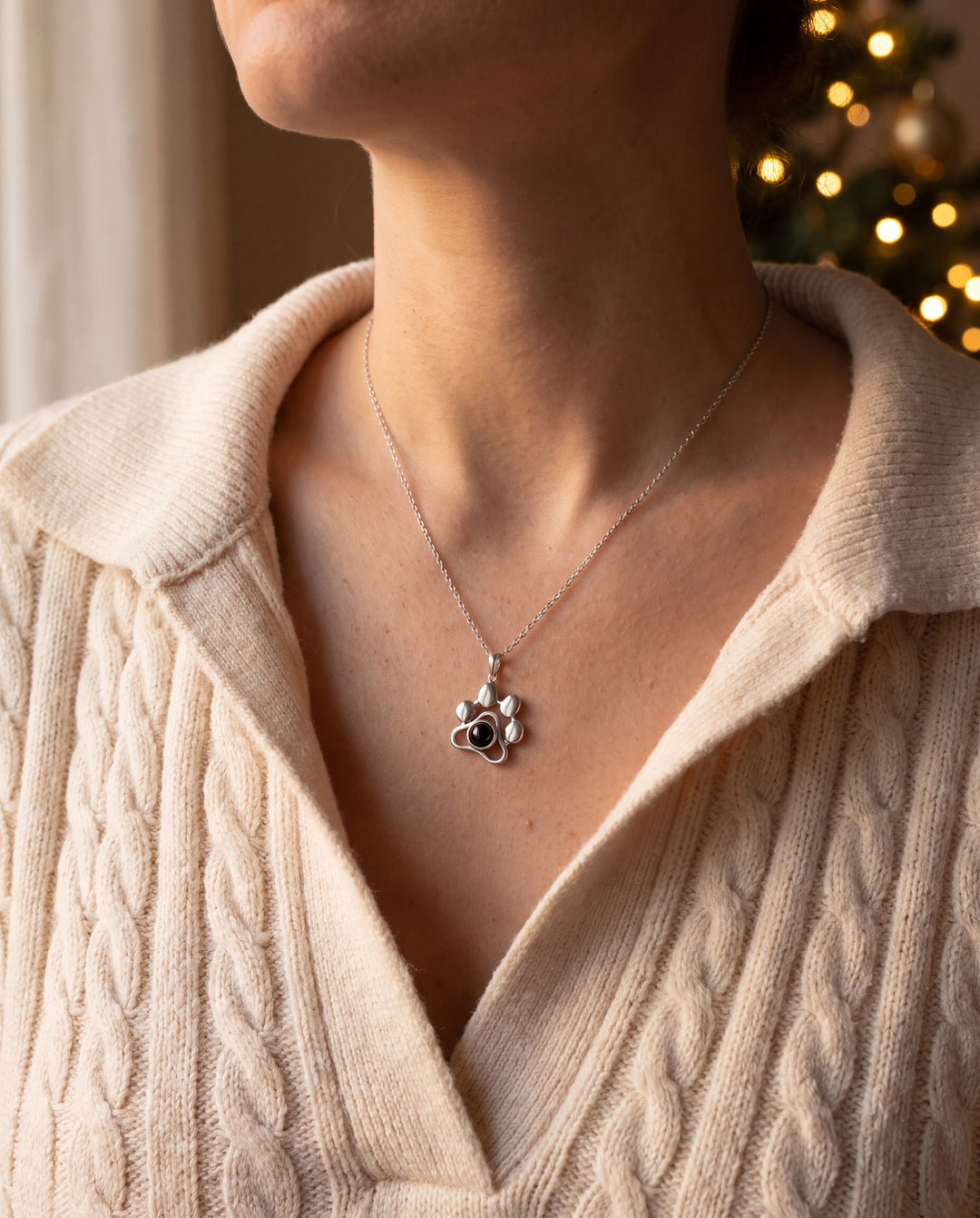 Woman wearing the silver paw projection necklace with a cream sweater