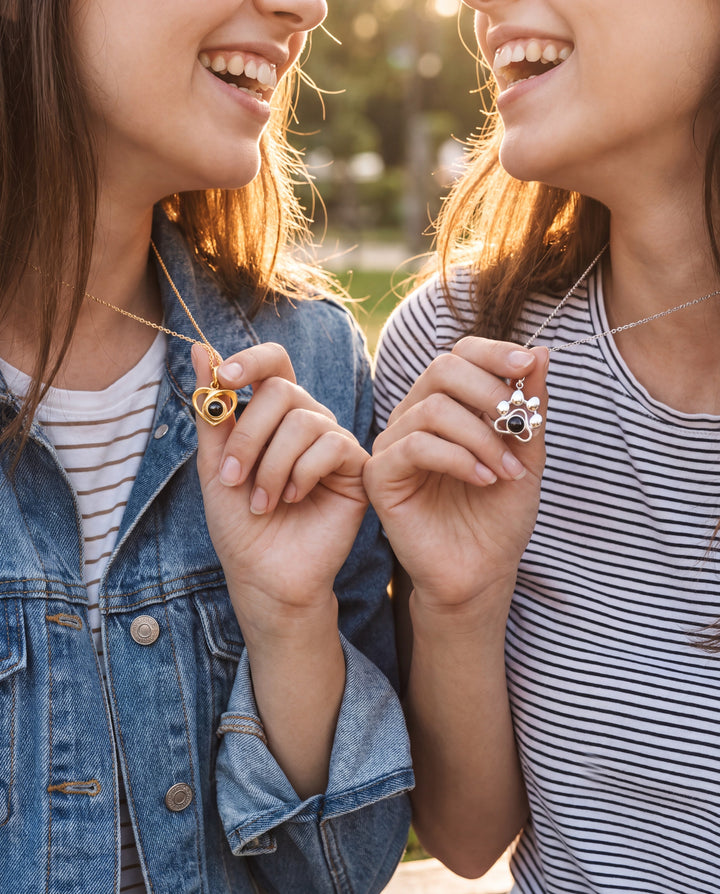 Two best friends laughing and holding up their matching projection necklaces